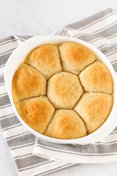 a white bowl filled with biscuits on top of a striped cloth