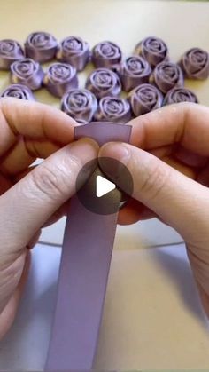 two hands are holding a purple ribbon in front of some rolled up flowers on a table