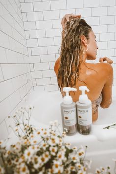 a woman sitting in a bathtub with two bottles of shampoo next to her