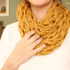 a woman wearing a yellow knitted cowl with her hands on her chest,