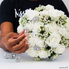 a woman holding a bouquet of white roses and diamond brooches in her hands