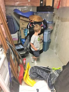 a young boy standing in the corner of a room filled with clutter and luggage