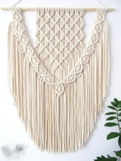 a macrame wall hanging on a white wall next to a potted plant