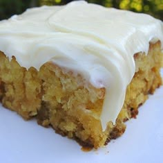 a close up of a piece of cake on a plate with white frosting and trees in the background