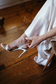 a woman in white dress and high heeled shoes sitting on a wooden floor next to a cat