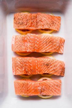 four salmon fillets in a baking dish with lemon slices and seasoning on top