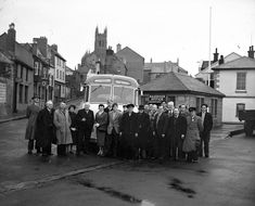 a group of people standing in front of a bus on a street next to buildings