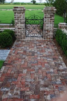 a brick walkway with an iron gate leading into the back yard and green grass in the background