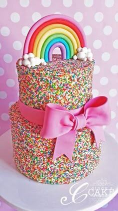 a rainbow cake with sprinkles on top and a bow at the bottom