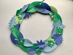 a paper wreath made to look like leaves and flowers is displayed on a white surface