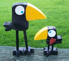 two black and yellow birds are standing next to each other on a wooden table in the grass