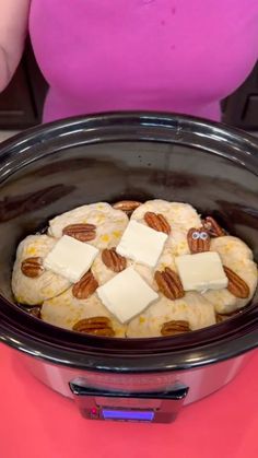 a woman in pink shirt standing next to a crock pot with cheese and nuts on it