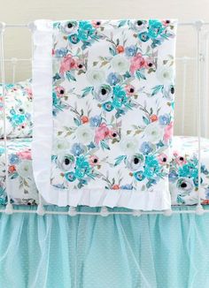 a white crib bed with blue and pink flowers on the sheets, along with matching pillow shampoos