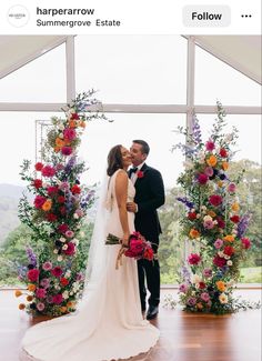 a bride and groom kissing in front of colorful floral archs at their wedding ceremony