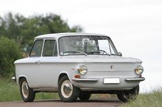 an old white car parked on the side of a road next to grass and trees