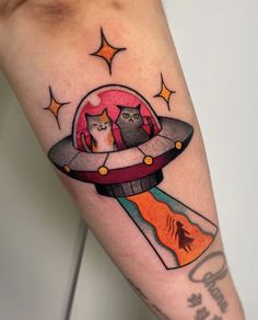 a tattoo with two cats in an alien spaceship on the arm, and stars above it