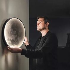 a man holding a large object in his right hand and looking at the moon behind it