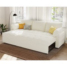 a white couch with yellow pillows in front of a window and rug on the floor