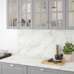 a kitchen with gray cabinets and white marble counter tops, along with a potted plant