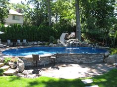 an above ground pool surrounded by rocks and water features a slide in the back yard