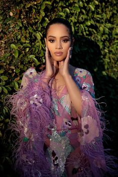 a woman with her hands on her face and wearing a purple feathered dress in front of bushes