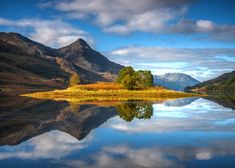 a lake surrounded by mountains with trees in the foreground and clouds in the sky