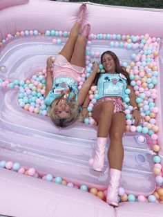 two women laying in an inflatable pool with balls on the floor and one wearing pink boots