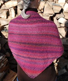 a woman with grey hair wearing a pink knitted shawl in front of stacks of wood