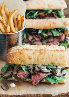 two sub sandwiches with meat, mushrooms and lettuce on them next to french fries