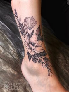 a woman's foot with flowers and leaves on the bottom of her leg,