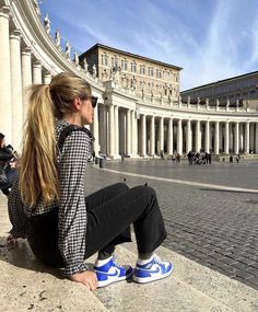 a woman sitting on the ground in front of a building with columns and arches around her