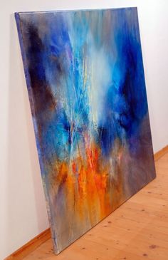 an abstract painting with blue, orange and yellow colors on a white wall next to a wooden floor