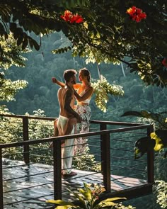 two women standing on a deck in front of some trees and flowers, one is brushing her hair