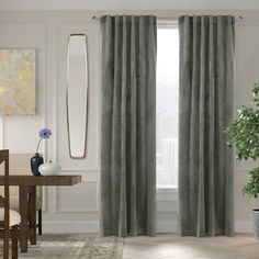 a living room with a table, chair and large window covered in grey drapes