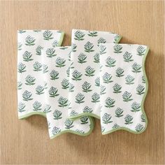 three napkins with green leaves on them sitting on top of a wooden table next to each other