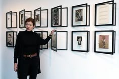 a woman standing next to a wall with framed pictures on it