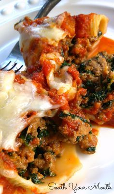 a white plate topped with lasagna and meat covered in sauce, cheese and spinach