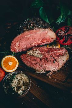 meat and vegetables on a cutting board with oranges, herbs and seasoning next to it