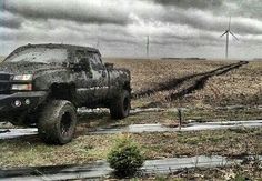 a black truck driving down a dirt road next to wind mills in the distance on a cloudy day