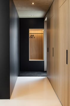 an empty hallway with black walls and wooden cabinets on either side, leading to the closets