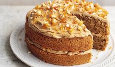 a cake with frosting and nuts on top sitting on a white plate next to a slice cut from the cake