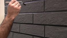 a man is painting the side of a brick wall with a paintbrush and glue