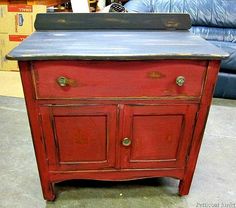 an old red cabinet with a black top and metal pulls on the bottom, in front of a blue couch