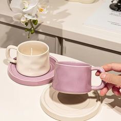 a person is holding a coffee cup and saucer on a white table with flowers in the background