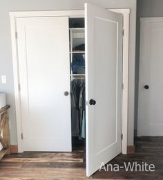 an open white closet with clothes hanging on the door and shelves in front of it