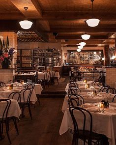 an empty restaurant with tables and chairs covered in white tablecloths, lit by candles