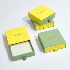 three small boxes are sitting next to each other on a white surface, one is yellow and the other is green