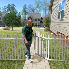 a man leaning against a white fence in front of a house and looking at the ground