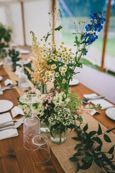 the table is set with glass vases, plates and flowers in them for a wedding reception