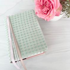 a pink flower sitting on top of a white table next to a green and blue notebook